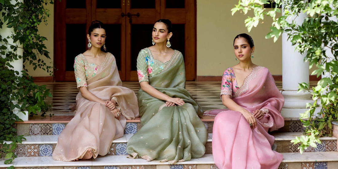 Women wearing elegant party wear organza sarees with delicate floral hand embroidery in pastel pink, sage green, and ivory colours.